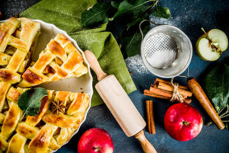 Traditional autumn baking, homemade apple pie with cinnamon, dark blue background with rolling roll, sugar powder, fresh apples, spices, copy space top viewの写真素材