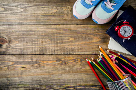 Back to school concept with kids sneakers, books, color pencils and alarm clock, wooden desk background top view copy spaceの写真素材