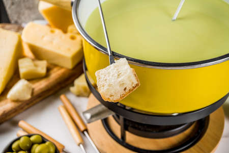 Gourmet Swiss fondue in traditional fondue pot, with forks, various cheeses, olives, bread and grape, white marble background copy spaceの写真素材