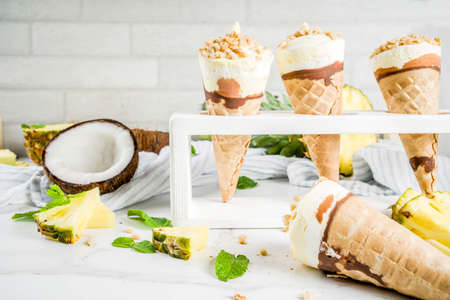 Tropical fruit homemade ice cream, with pineapple and coconut, waffle crumbs, on a white marble...