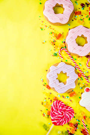 Sweets creative lay out, dessert concept with lollipops, jellies, candy, cookies donuts and cupcakes, bright yellow background top view copy spaceの写真素材