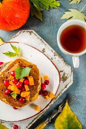 Autumnal breakfast idea, pumpkin pancakes, with slices of pumpkin, maple syrup or honey, cranberry, on a blue concrete background, space for textの写真素材