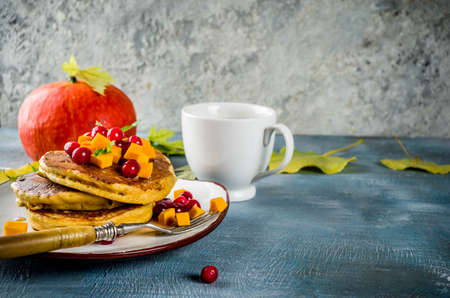 Autumnal breakfast idea, pumpkin pancakes, with slices of pumpkin, maple syrup or honey, cranberry, on a blue concrete background, space for textの写真素材