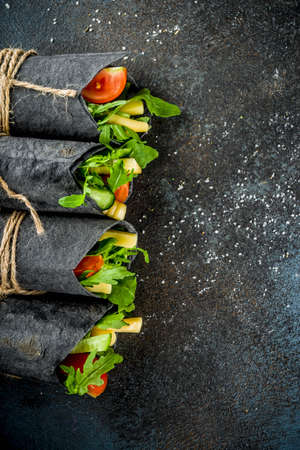 Trendy healthy vegan food. Black charcoal wrapped sandwiches, with fresh vegetables, cheese, on a dark blue background, space for textの写真素材