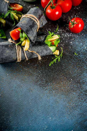 Trendy healthy vegan food. Black charcoal wrapped sandwiches, with fresh vegetables, cheese, on a dark blue background, space for textの写真素材
