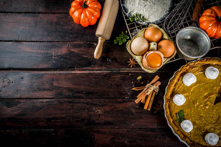 Autumn baking background, baking ingredients for pies, cookies - pumpkins, pumpkin pie, spices, flour, eggs, rolling pin, whisk, old wooden table top view copy space, with notebook for recipesの写真素材