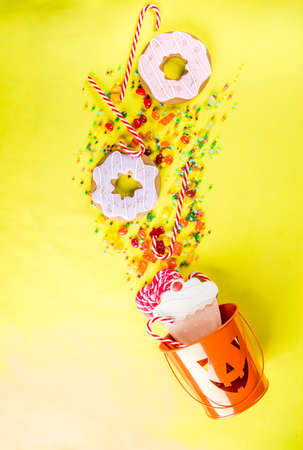 Halloween sweets concept, bucket in the form of a festive pumpkin, full of sweets and candies, cookies, jellies, desserts, bright yellow background top view copy spaceの写真素材