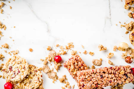 Multi grain granola muesli bar. Healthy sweet food, diet snack, with dried berries, nuts, cereals and honey. On a white marble background, top view copy place for text.の写真素材