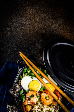 Traditional asian food, ramen soup with shrimp, noodles, spring onion, sliced eggs, mushrooms, on dark concrete background with chopsticks copy space top viewの写真素材