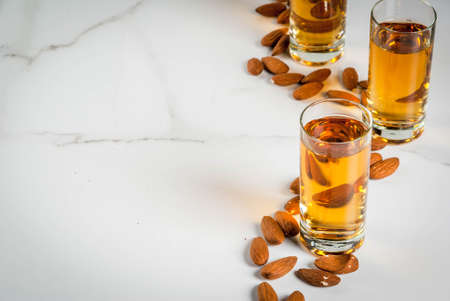 Golden almond liqueur with nuts on white marble background. copy space