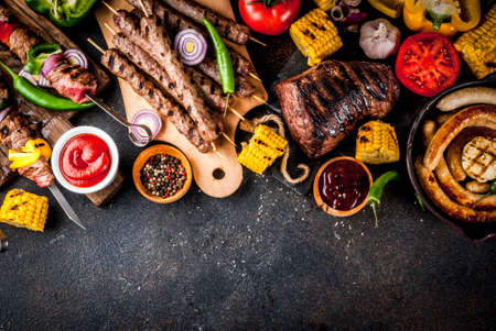 Assortment various barbecue food grill meat, bbq party fest - shish kebab, sausages, grilled meat fillet, fresh vegetables, sauces, spices, dark rusty concrete table, above copy spaceの写真素材