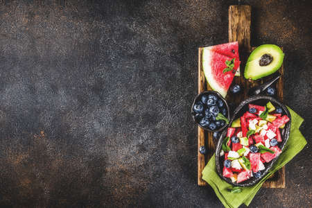 Summer food concept, fresh cold watermelon salad with feta cheese, blueberry, avocado and mint, dark...