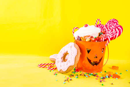 Halloween sweets concept, bucket in the form of a festive pumpkin, full of sweets and candies,...