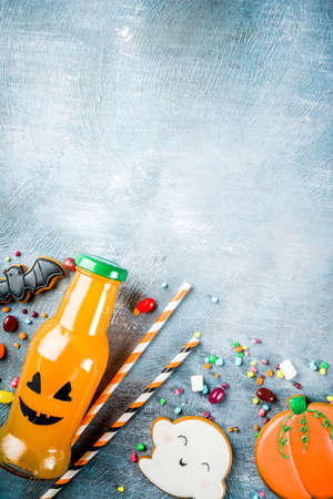 Kids treats for Halloween, funny homemade glazed cookies, various candies milk and juice in monster bottle, blue concrete background copy space top viewの写真素材