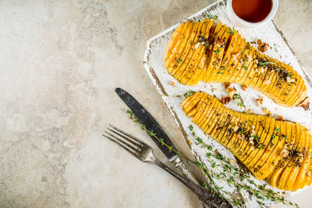 Simple autumn domestic recipes, roasted hasselback butternut squash pumpkin with thyme, honey and maple syrup, on light background copy space top viewの写真素材