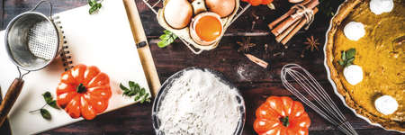 Autumn baking background, baking ingredients for pies, cookies - pumpkins, pumpkin pie, spices, flour, eggs, rolling pin, whisk, old wooden table top view copy space, with notebook for recipes bannerの写真素材