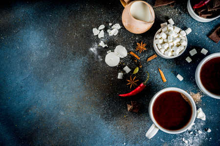 Hot chocolate cups, broken pieces of chocolate, sugar, marshmallow, red chili peppers and spices. Dark blue concrete background top view spaceの写真素材