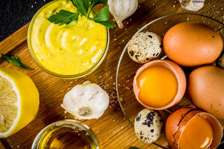 Homemade mayonnaise sauce with ingredients - lemon, eggs, olive oil, spices and herbs, black concrete background copy spaceの写真素材