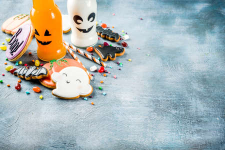 Kids treats for Halloween, funny homemade glazed cookies, various candies milk and juice in monster bottle, blue concrete background copy space top viewの写真素材