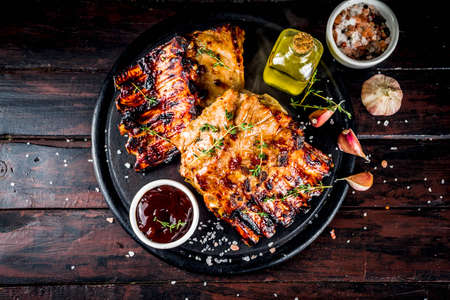 Grilled meat concept. bbq pork ribs with barbeque sauce, olive oil. fresh herbs on dark wooden background copy spaceの写真素材