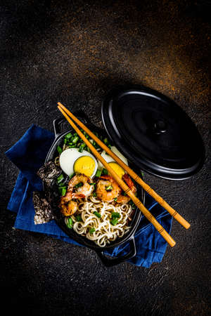 Traditional asian food, ramen soup with shrimp, noodles, spring onion, sliced eggs, mushrooms, on dark concrete background with chopsticks copy space top viewの写真素材