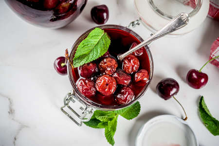 Homemade preserved cherry and mint jam, with fresh cherries on white marble background copy space...