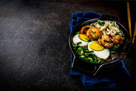 Traditional asian food, ramen soup with shrimp, noodles, spring onion, sliced eggs, mushrooms, on dark concrete background with chopsticks copy space top viewの写真素材