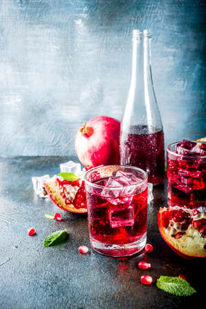 Fall cold beverage ideas, pomegranate cocktail, sparkling water with mint and ice cubes, dark blue background copy spaceの写真素材