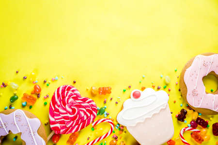 Sweets creative lay out, dessert concept with lollipops, jellies, candy, cookies donuts and cupcakes, bright yellow background top view copy spaceの写真素材