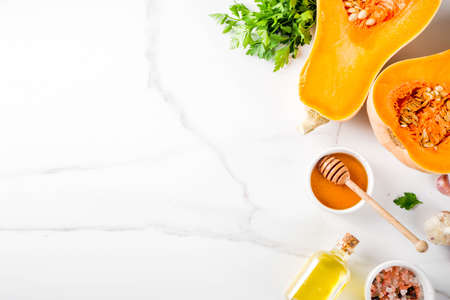 Halves of raw pumpkin or butternut squash, with olive oil, spices and ingredients for cooking on white marble background.Top view copy space.の写真素材