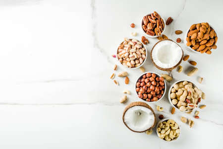 Various types of nuts - walnuts, pecans, peanuts, hazelnuts, coconut, almonds, cashews, in bowls, on a white marble table top viewの写真素材