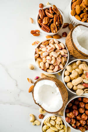 Various types of nuts - walnuts, pecans, peanuts, hazelnuts, coconut, almonds, cashews, in bowls, on a white marble table top viewの写真素材