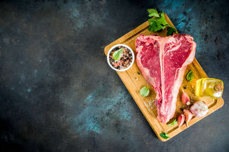 Raw fresh meat, t-bone beef steak with spices and herbs on cutting board, concrete table top view copy spaceの写真素材