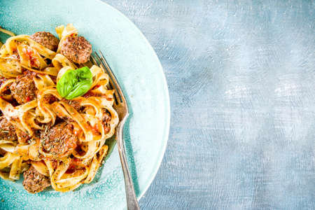 Italian fettuccine pasta with meatballs in tomato sauce in a portioned plate on light blue concrete background.Top view copy spaceの写真素材