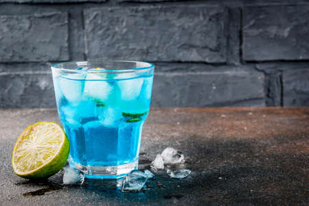 Colorful summer beverage, iced blue  alcohol cocktail drink with lime and mint, bark background copy spaceの写真素材
