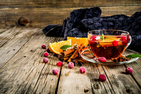 Autumn winter hot drink, cranberry spicy tea with orange, cinnamon and anise. On an old wooden background, with a warm blanket, copy space for textの写真素材