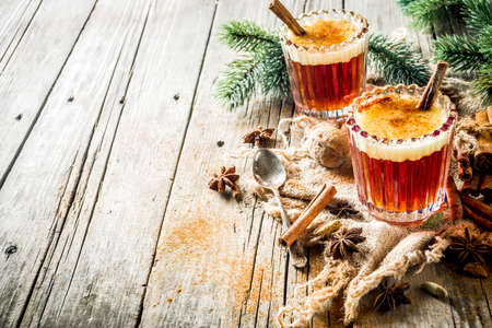 Winter holidays traditional drink, homemade hot buttered rum with spices, over old rustic wooden background with christmas tree branches, copy spaceの写真素材