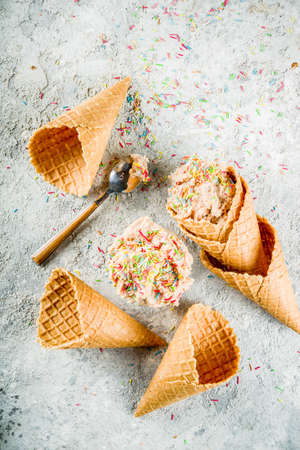 Edible Raw Cookie Dough, sweet modern dessert, with waffle ice cream cones on grey stone background,...