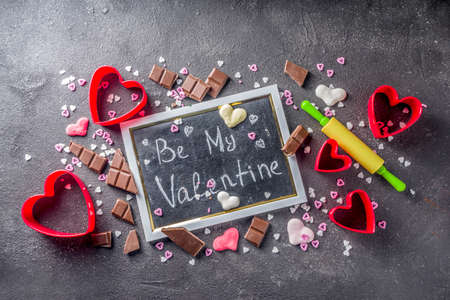 Valentine day baking concept, sweets and baking cooking background for Valentine`s day, with rolling pin, cookie cutters, sugar sprinkling, chocolate. Black concrete table top view copy spaceの写真素材