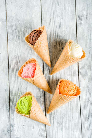 Colorful ice cream in waffle ice cream cones, sweet homemade summer dessert, old wooden background...