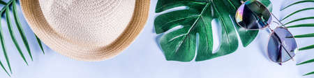 Colorful summer vacation and holiday flat-lay. Straw hat, sunglasses, palm and monstera leaves on bright blue yellow background, top view, copy space bannerの写真素材