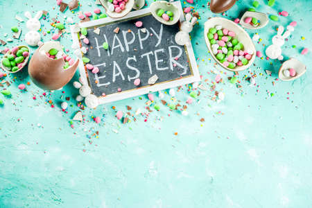 Colorful spring easter sweets background, with chocolate eggs, sugar sprinkles and marshmallow bunny, turquoise light blue concrete background copy space top viewの写真素材