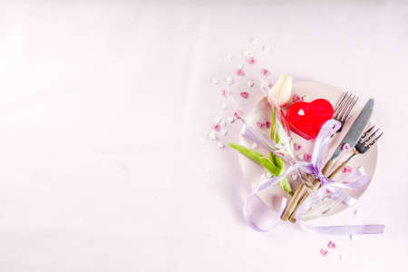 Festive table setting for Valentine's Day with cutlery, flower, gift box and confetti hearts on pink...