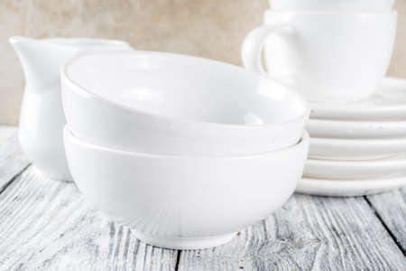 Assortment stack clean empty new white kitchen utensils, plates, bowls, cups mugs. On a white...