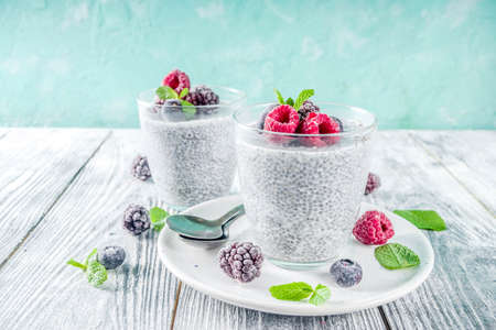 Summer healthy breakfast dessert in glass, overnight vegan chia pudding with non-dairy milk, frozen raspberry, blackberry and blueberry, on light blue and wooden background copy spaceの写真素材