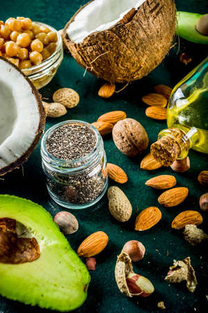 Healthy vegan fat food sources, omega3, omega6 ingredients - almond, pecan, hazelnuts, walnuts, olive oil, chia seeds, avocado, coconut, dark green background copy spaceの写真素材