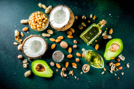 Healthy vegan fat food sources, omega3, omega6 ingredients - almond, pecan, hazelnuts, walnuts, olive oil, chia seeds, avocado, coconut, dark green background copy spaceの写真素材
