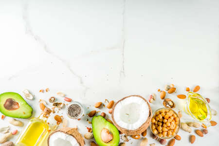 Healthy vegan fat food sources, omega3, omega6 ingredients - almond, pecan, hazelnuts, walnuts, olive oil, chia seeds, avocado, coconut, dark green background copy spaceの写真素材