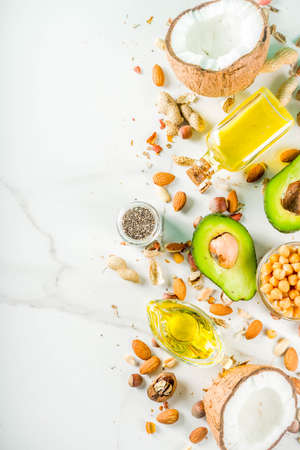 Healthy vegan fat food sources, omega3, omega6 ingredients - almond, pecan, hazelnuts, walnuts, olive oil, chia seeds, avocado, coconut, dark green background copy spaceの写真素材