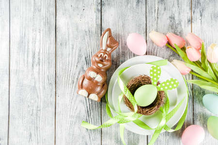 Easter holiday table setting with rabbits and eggs, plates with colorful eggs and chocolate bunny...
